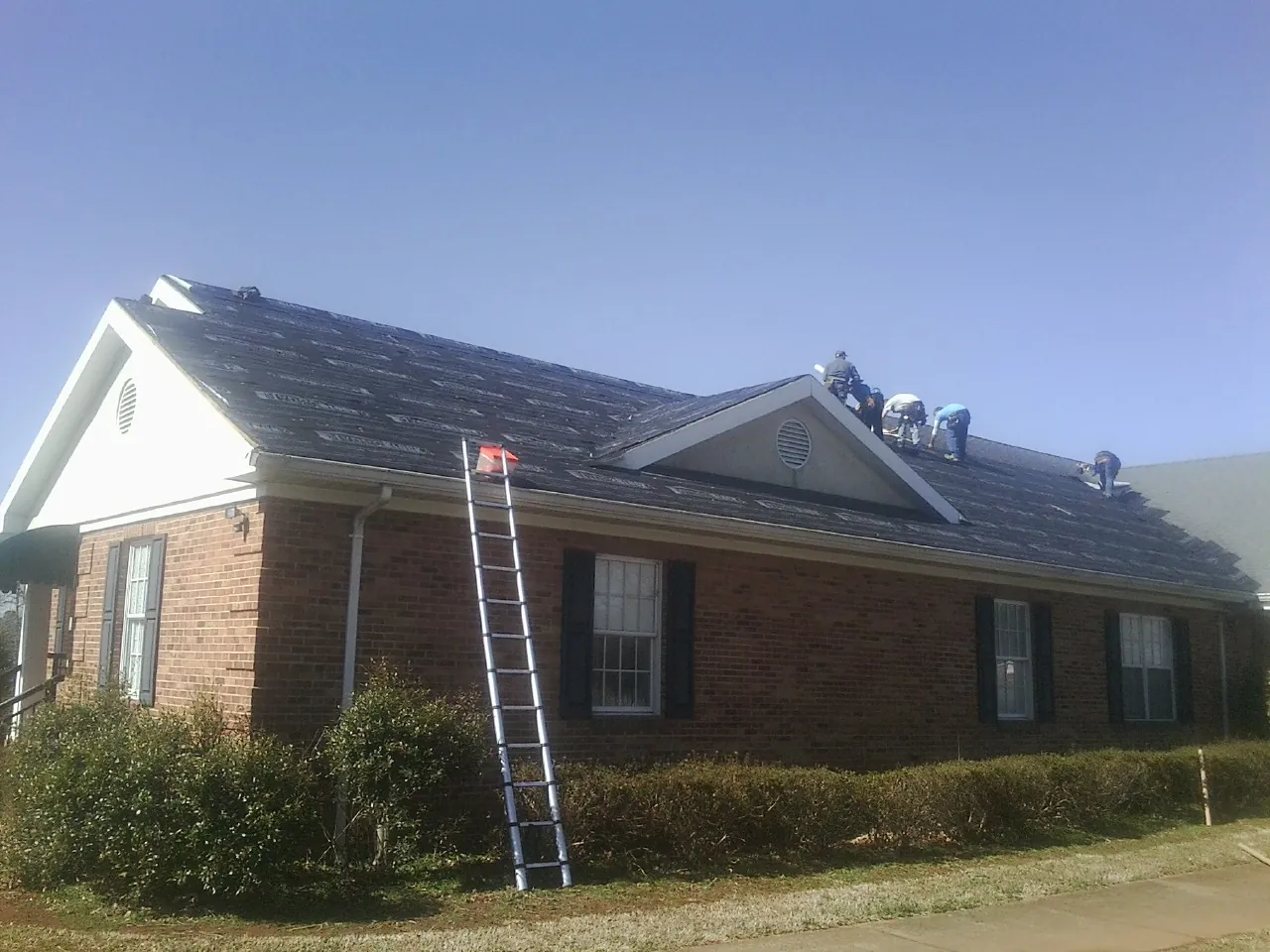 Crew tearing shingles off a brick ranch roof with a ladder set — Metal Roof Repair work by our crew in Fiskdale
