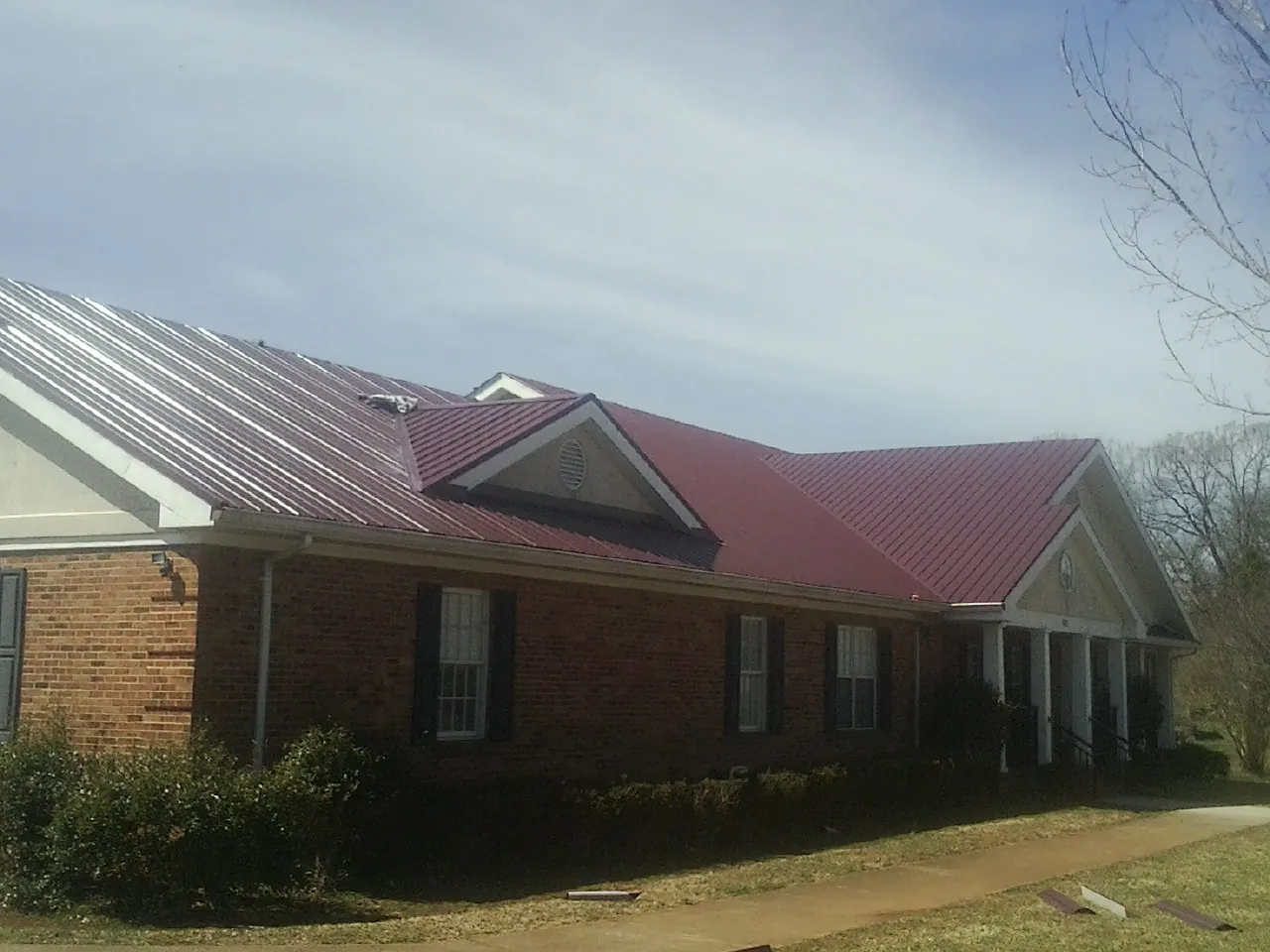 Red metal roof with gabled entries on a long brick building, from a Hail Damage Roof Repair job in Fiskdale