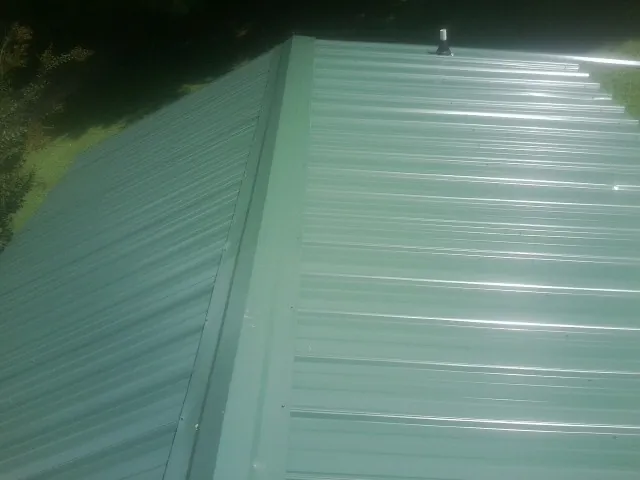 New green metal panels meeting at the ridge of a roof — Flat Roof Repair work by our crew in Fiskdale