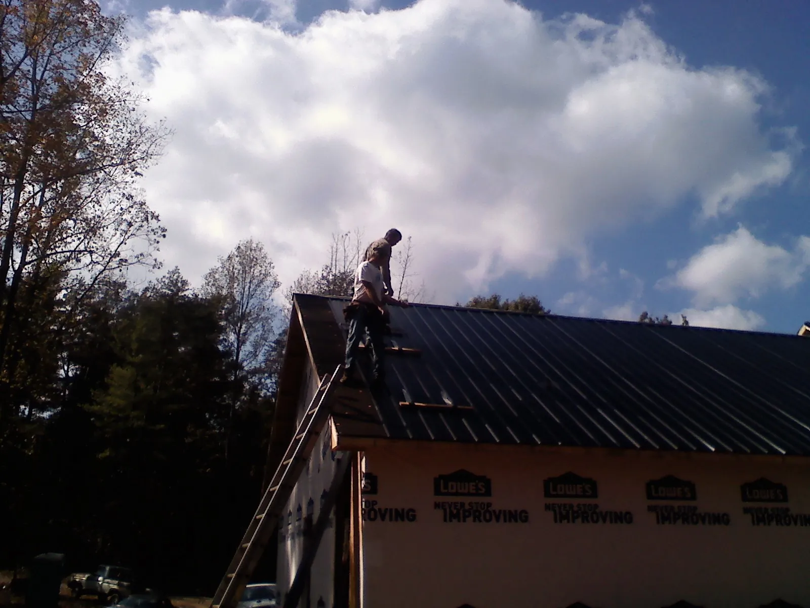 Roofer fastening dark metal panels high against a cloudy sky, from a Roof Inspection job in Fiskdale