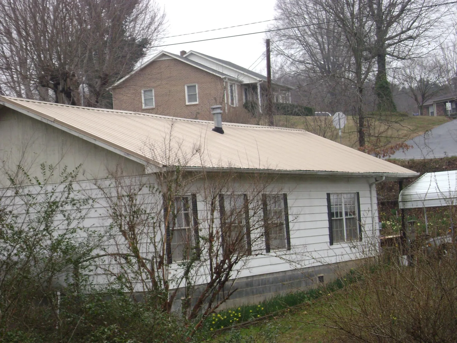 Tan metal roof on a white sided house set into a hillside — Commercial Roofing by Roofing Brothers in Fiskdale