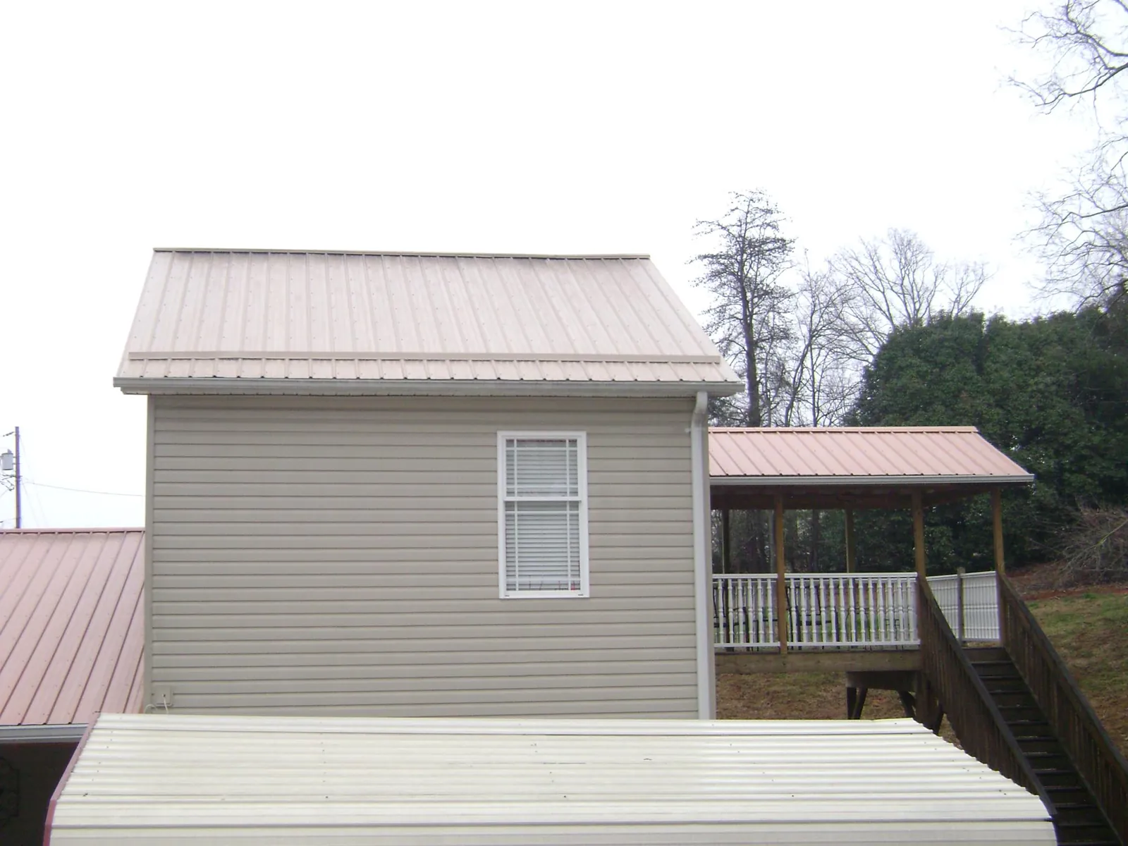 Tan metal roofs on a two story addition and attached porch, from a Roof Replacement job in Fiskdale